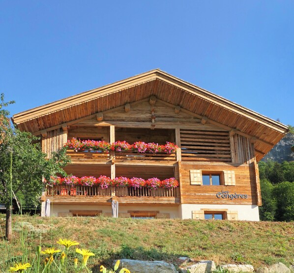 Una cabaña de madera con un balcón decorado con flores, frente a un paisaje montañoso.