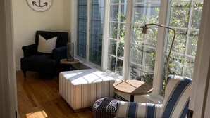 A sunlit room with a sofa, ottoman, and a chair near large windows.