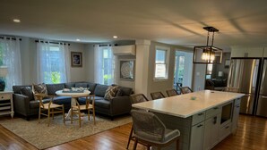 A modern kitchen with a central island, bar stools, and a dining area with a sofa and chairs.