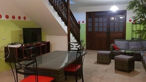 A dining area with a glass-top table and red cushioned chairs, a staircase, a sofa, and a television. - TITIRI apartment with terrace and garden (Sainte-Anne)