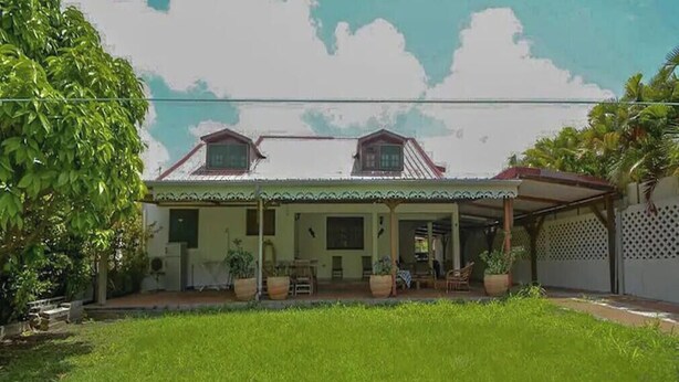 A two-story house with a covered porch and a garden. - TITIRI apartment with terrace and garden (Sainte-Anne)