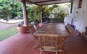 Une terrasse couverte avec une table et des chaises en bois, un hamac et des plantes en pot.