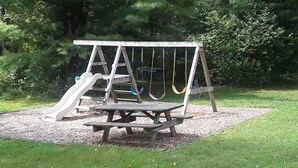 Een houten schommel met glijbaan en een picknicktafel in een park.
