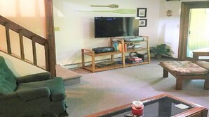 Een woonkamer met een groene bank, een houten salontafel, een televisie op een standaard en een trap die naar een ander niveau leidt.