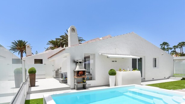 Una casa moderna amb piscina, zona de barbacoa i jardí ben cuidat.