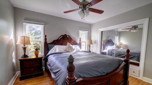 Un dormitorio con una cama de madera, dos mesitas de noche con lámparas, un ventilador de techo y un espejo grande.