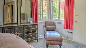 A bedroom with a bed, a dresser with mirrors, a chair, and a window with curtains.