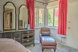 Quarto com cama, penteadeira com espelhos, cadeira e janela com cortinas.