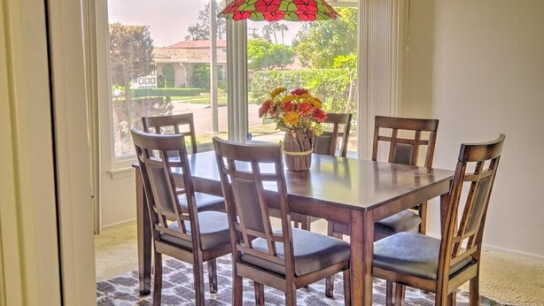 A dining area with a table and chairs, a vase with flowers, and a view of the outdoors.