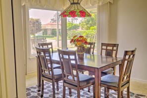 A dining area with a table and chairs, a vase with flowers, and a view of the outdoors.