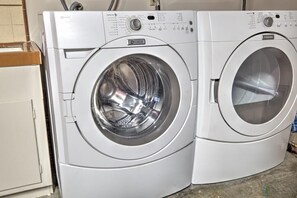 Vista frontal de uma máquina de lavar branca, com duas portas, painéis de controle e porta transparente.