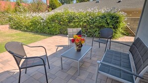 An outdoor patio with two metal chairs, a small table, and a vase of flowers.