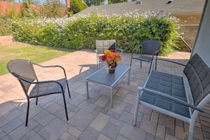 Um pátio externo com duas cadeiras de metal, uma mesa pequena e um vaso de flores.