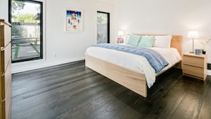 A bedroom with a large bed, wooden headboard, and a nightstand with a lamp. - Oak Haven (Altadena)