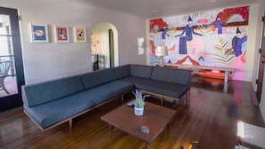 A modern living room with a sectional sofa, a coffee table with a plant, and a colorful abstract painting on the wall. - Oak Haven (Altadena)