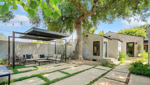A modern outdoor patio with a seating area, a pergola, and a small building with steps leading to a door. - Oak Haven (Altadena)