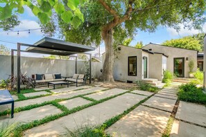 A modern outdoor patio with a seating area, a pergola, and a small building with steps leading to a door. - Oak Haven (Altadena)