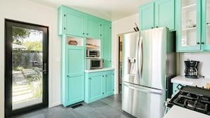 A modern kitchen with teal cabinets, a stainless steel refrigerator, and a gas stove. - Oak Haven (Altadena)