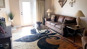 Ein Wohnzimmer mit einem braunen Ledersofa, einem Couchtisch, einem Teppich mit Halbmondmuster, einer Lampe und einem an der Wand befestigten Bilderrahmen.
