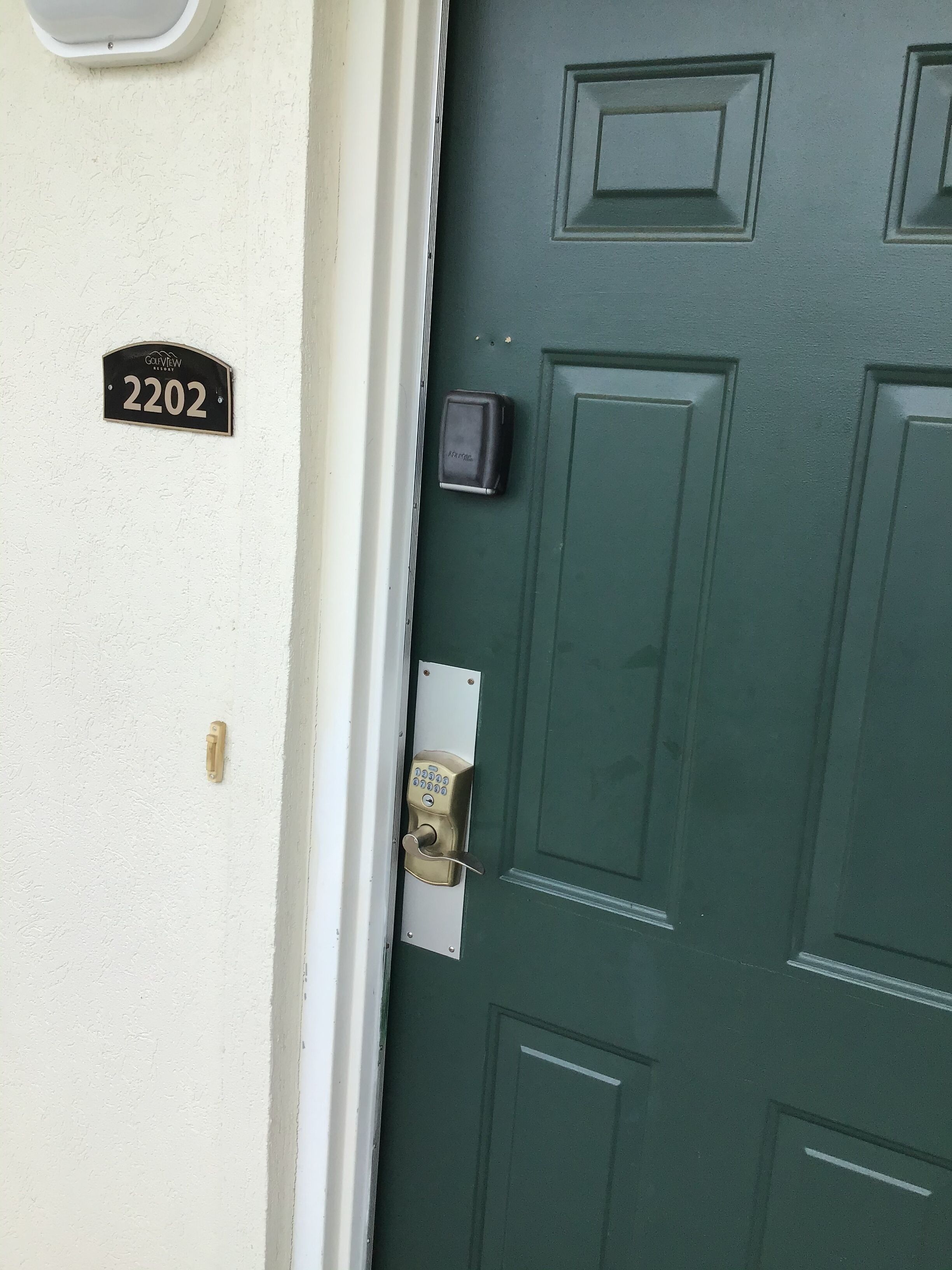 A green door with a keypad lock, a doorbell, and a house number sign.