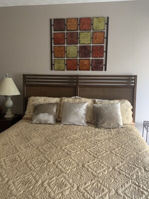Een bed met een quilt met patroon, een houten hoofdbord en een decoratief paneel aan de muur.