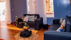 A modern living room with a sofa, a coffee table with a fruit bowl, and a large window with curtains. - Konga Hotel Kigali (Kigali)