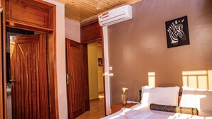 A hotel room with a wooden wardrobe, a bed with white linens, a zebra artwork on the wall, and an air conditioning unit. - Konga Hotel Kigali (Kigali)