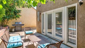 An outdoor patio with wicker furniture, a grill, and a sliding glass door leading to a backyard.