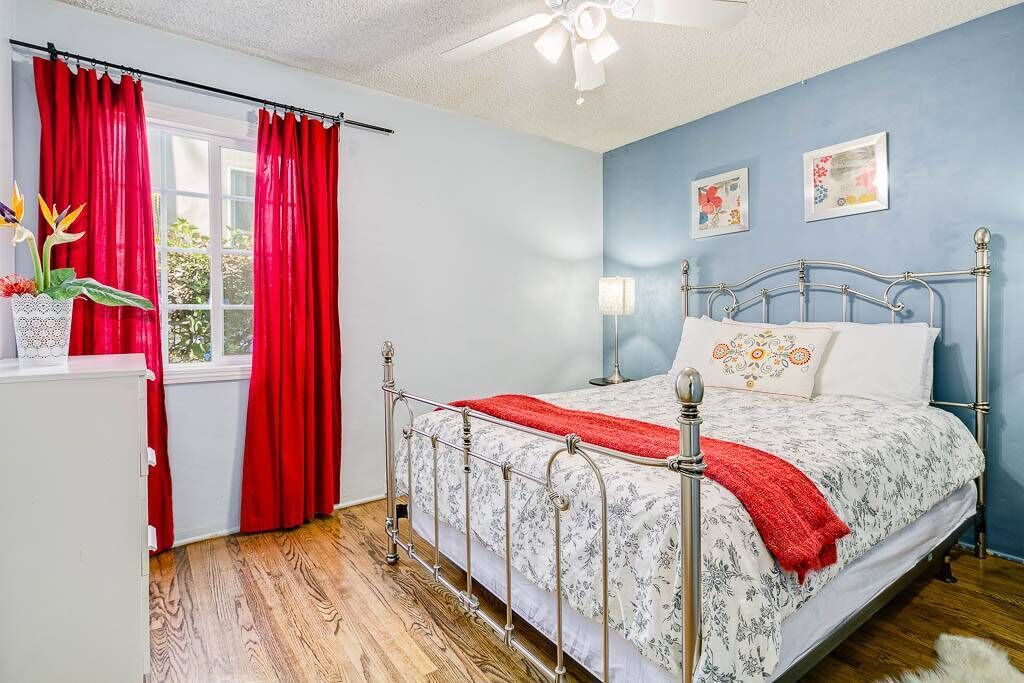 A bedroom with a metal bed frame, a red blanket, and a window with red curtains.