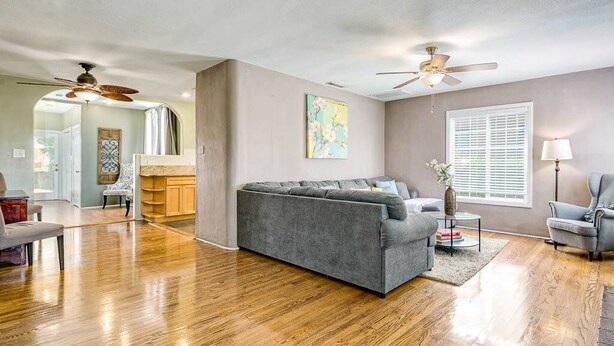 A spacious living room with hardwood flooring, a grey sofa, a coffee table, and a ceiling fan.