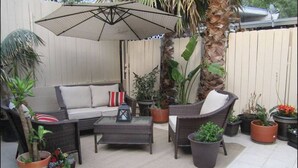 An outdoor patio area with wicker furniture, a glass-top coffee table, and various potted plants.