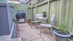 A patio area with a barbecue grill, two chairs, a small table, and a potted plant. - The Willows (Pasadena)
