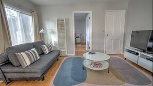 A modern living room with a grey sofa, a round coffee table, and a flat-screen TV. - The Willows (Pasadena)