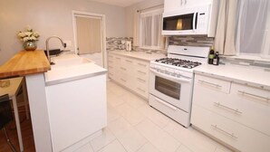 A modern kitchen with white cabinets, a gas stove, a microwave, and a sink. - The Willows (Pasadena)