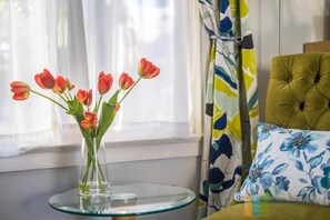 Una mesa de vidrio con un jarrón de tulipanes rojos, una silla tapizada de verde y un cojín floral.