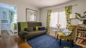 A modern living room with a sofa, armchair, and a small table with a vase of flowers. - The Sycamore (Pasadena)