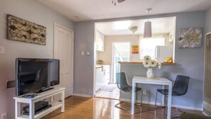 A living room with a TV on a stand, a dining table with chairs, and a kitchen visible through an open door. - The Sycamore (Pasadena)