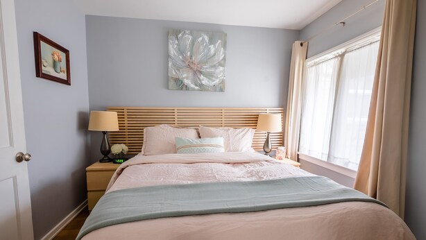 A neatly arranged bedroom with a bed, bedside tables, a lamp, and a painting on the wall. - The Deodora (Pasadena)