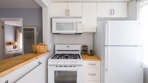 A modern kitchen with white cabinetry, a gas stove, a microwave, and a refrigerator. - The Deodora (Pasadena)