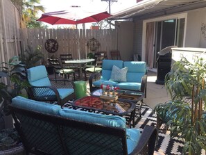 A patio with outdoor furniture, including a sofa, chairs, and a table, surrounded by plants and a wooden fence. - Juniper House (Altadena)