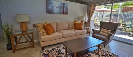 Ein Wohnzimmer mit einem beigen Sofa, einem Holztisch und einem gemusterten Teppich.