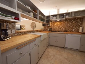 A modern kitchen with white cabinets, a wooden countertop, and a tiled backsplash. - Juniper House (Altadena)