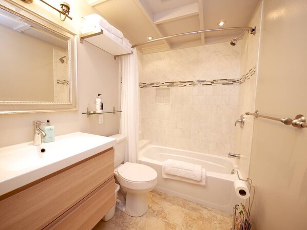 A modern bathroom with a large mirror, a white sink, a toilet, and a bathtub. - Juniper House (Altadena)