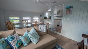 A living room with a beige sofa, patterned cushions, a ceiling fan, and a view into the kitchen. - Palm Terrace (Delray Beach)