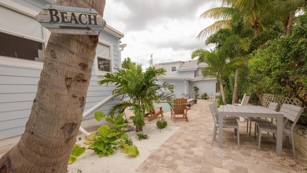 A patio area with a wooden table and chairs, surrounded by plants and a sign pointing to the beach. - Palm Terrace (Delray Beach)