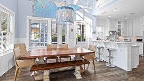 A spacious kitchen with white cabinetry, a central island with stools, and a large dining table with chairs. - Luxury Watersound Getaway with Golf Cart (Watersound)
