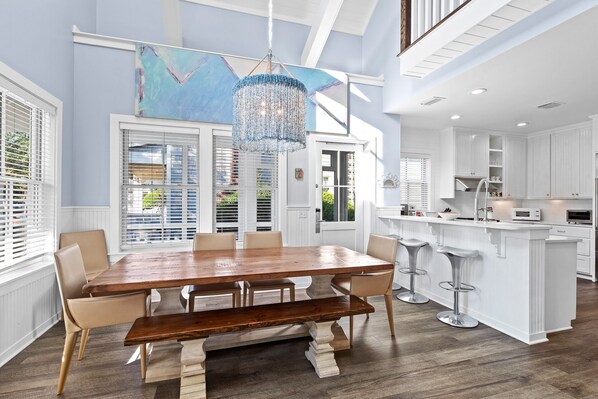 A spacious kitchen with white cabinetry, a central island with stools, and a large dining table with chairs.
