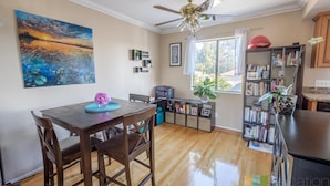 A dining area with a wooden table and chairs, a ceiling fan, a bookshelf, and a window with curtains. - The Madison (Pasadena)