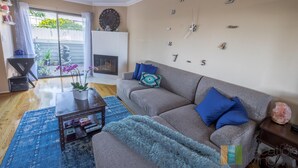 A living room with a grey sofa, blue cushions, a blue rug, a coffee table, and a wall clock. - The Madison (Pasadena)