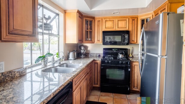 A modern kitchen with granite countertops, wooden cabinets, a stainless steel refrigerator, a black stove, and a microwave. - The Madison (Pasadena)